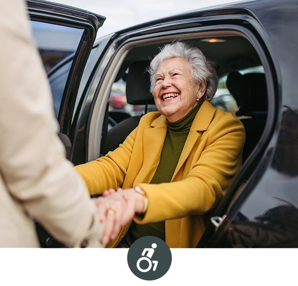 Ältere Dame steigt aus dem Auto, Pflegekraft hilft ihr und hält ihre Hände.